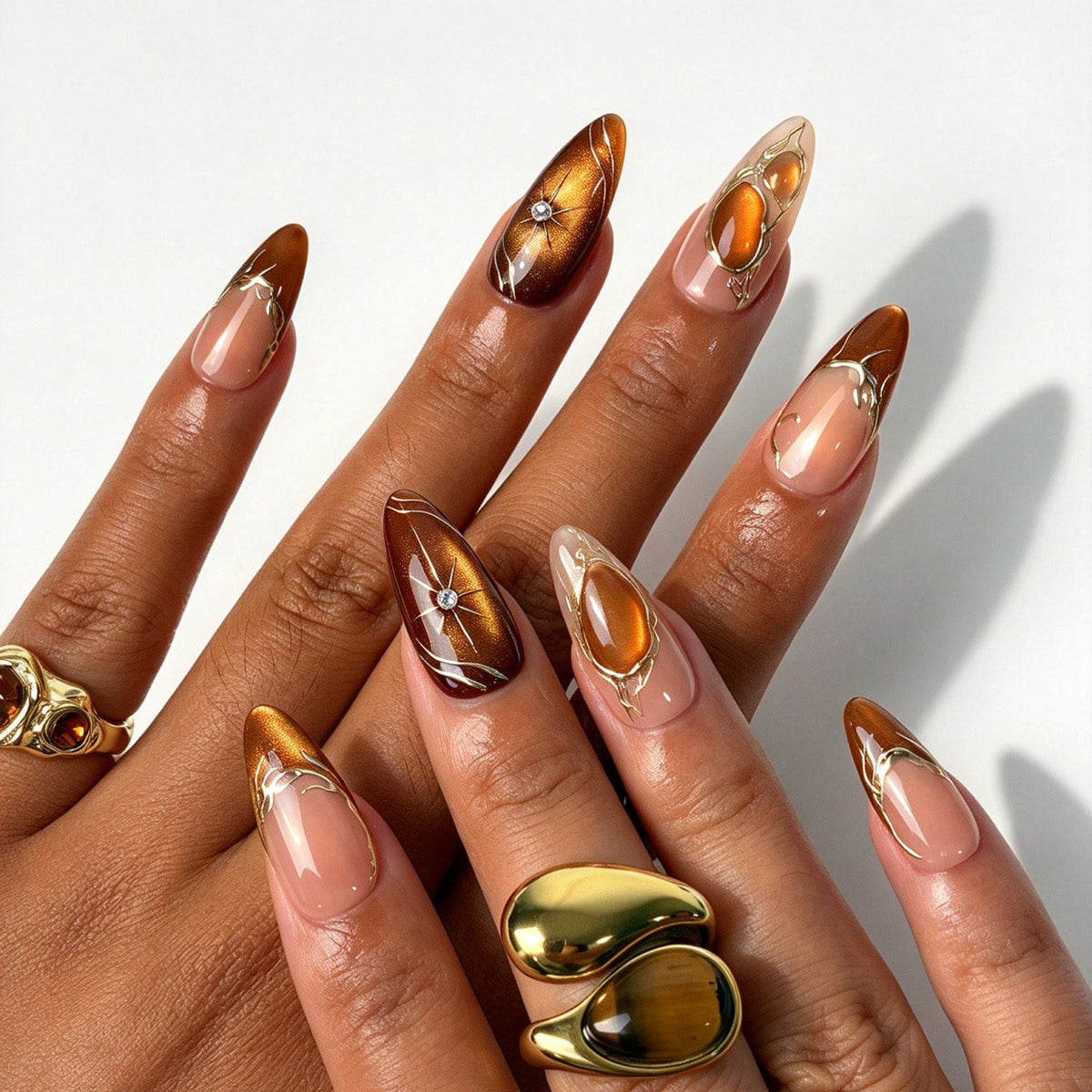Luxe almond false nails, amber cat eye nude gradient with hand drawn gold cracked lines and star rhinestones