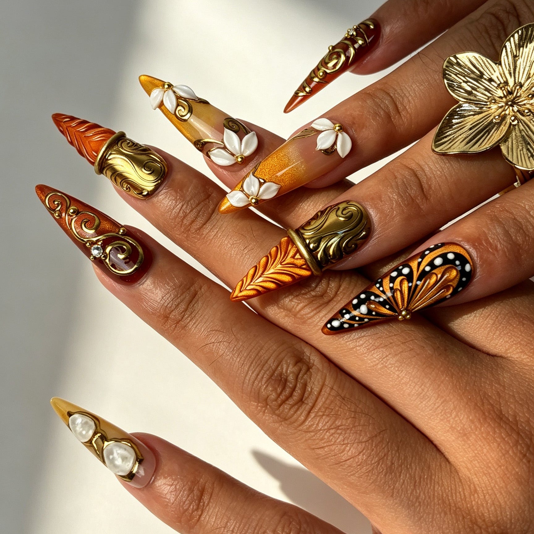 Close‑up of long stiletto false nails, 3D white flower and carved gold‑leaf autumn design