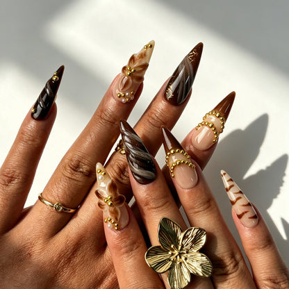Model hands with Mocha Bloom vintage press‑on nails, stiletto shape coffee brown marble 3D floral gold decorations