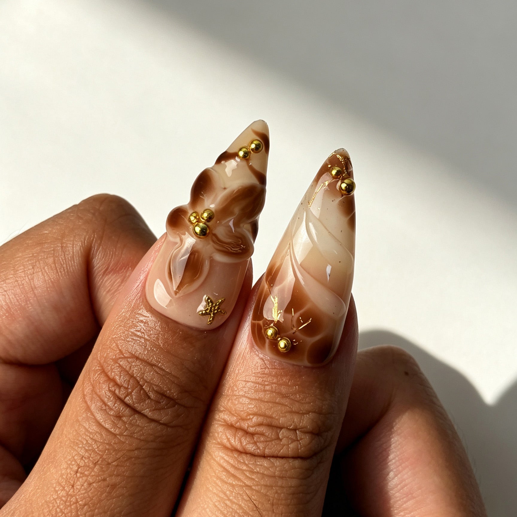 Close‑up view of Mocha Bloom stiletto false nails, coffee brown marble 3D flower gold bead chain design
