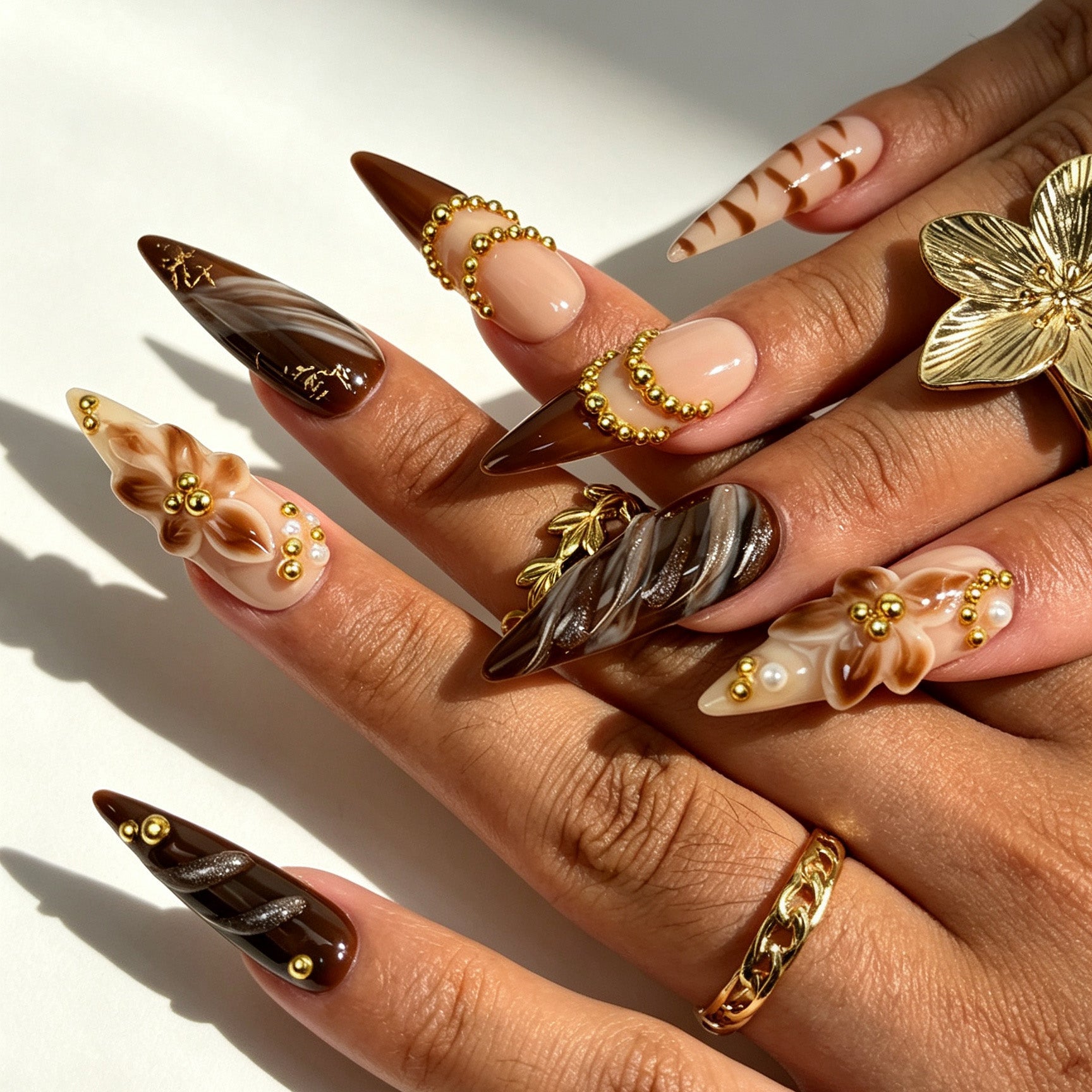 Close‑up of hands wearing Mocha Bloom handmade stiletto press‑on nails, brown marble 3D flower gold chain nail art