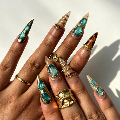 Boho‑luxury stiletto press‑on nails with turquoise cat‑eye gem and rhinestones on hand
