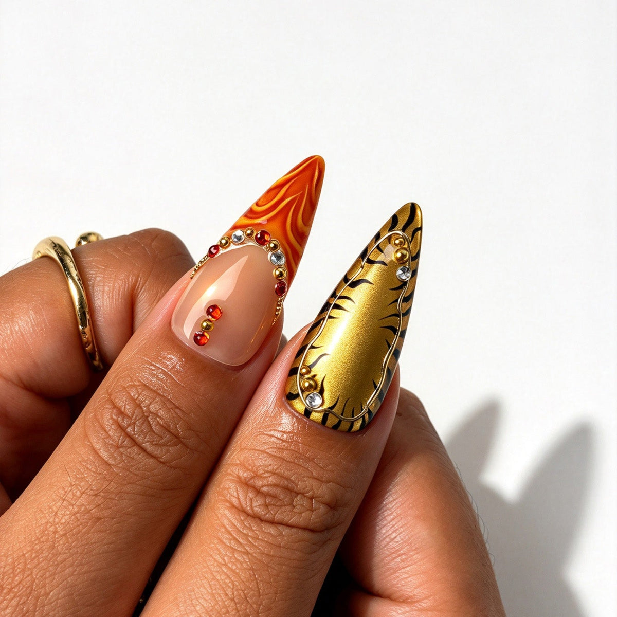 Closeup of Wild Amber stiletto nails, tiger print, orange swirl art, gold metal beads and red rhinestones