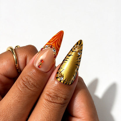 Closeup of Wild Amber stiletto nails, tiger print, orange swirl art, gold metal beads and red rhinestones