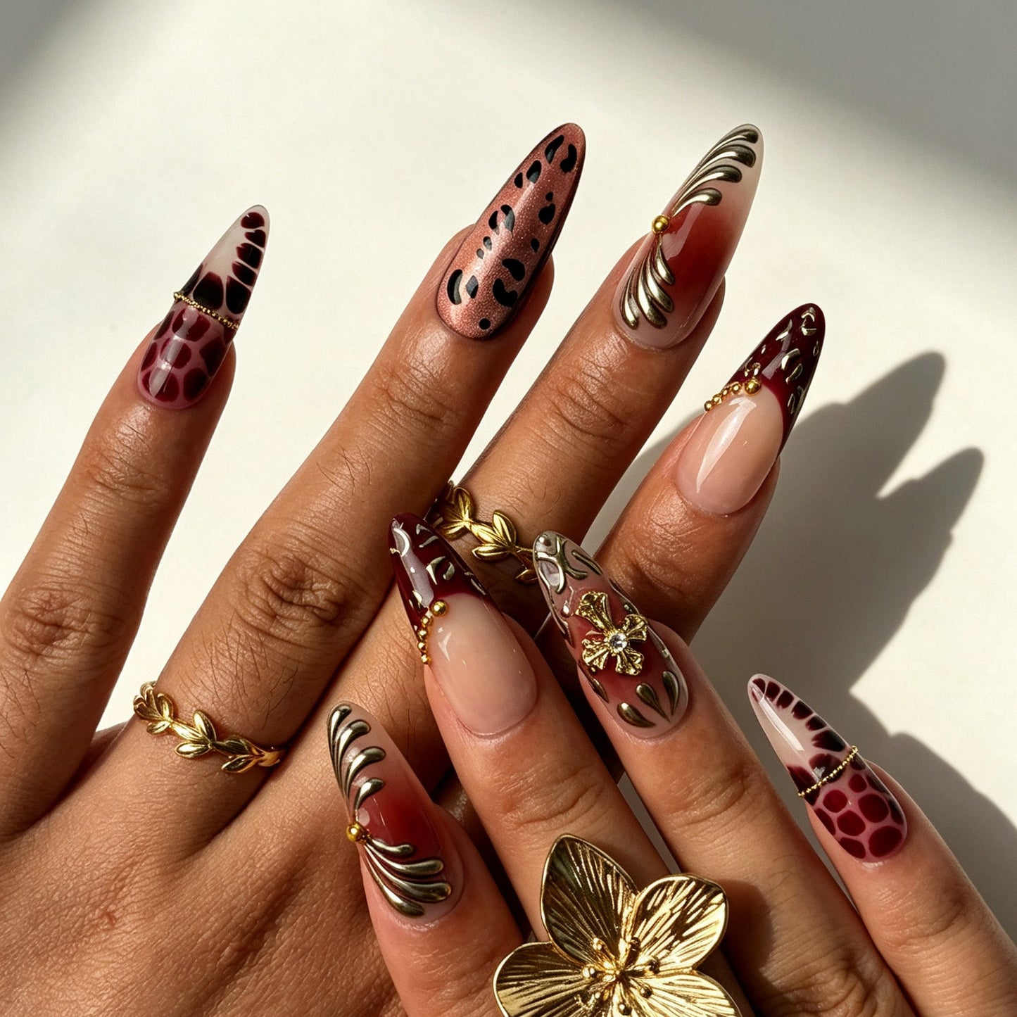 Model hands with Wine Felis vintage press‑on nails, long almond wine‑red with gold cross & leopard print
