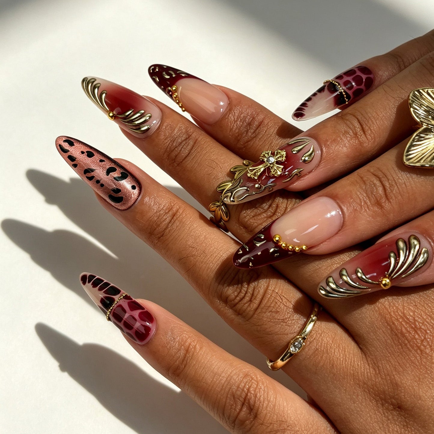 Hands wearing Wine Felis handmade almond press‑on nails, wine‑red gold cross leopard tortoiseshell nail art